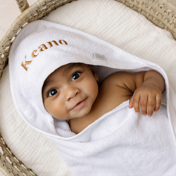 Baby gewikkeld in een gepersonaliseerde witte badcape met naam Keano geborduurd, ideaal als uniek en praktisch kraamcadeau.