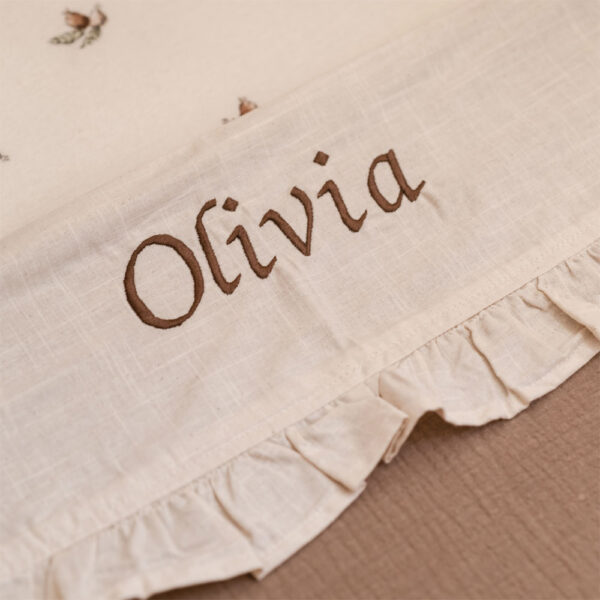 Gepersonaliseerd beige babylaken met bruine geborduurde naam ‘Olivia’ en elegante ruches, ideaal als kraamcadeau.