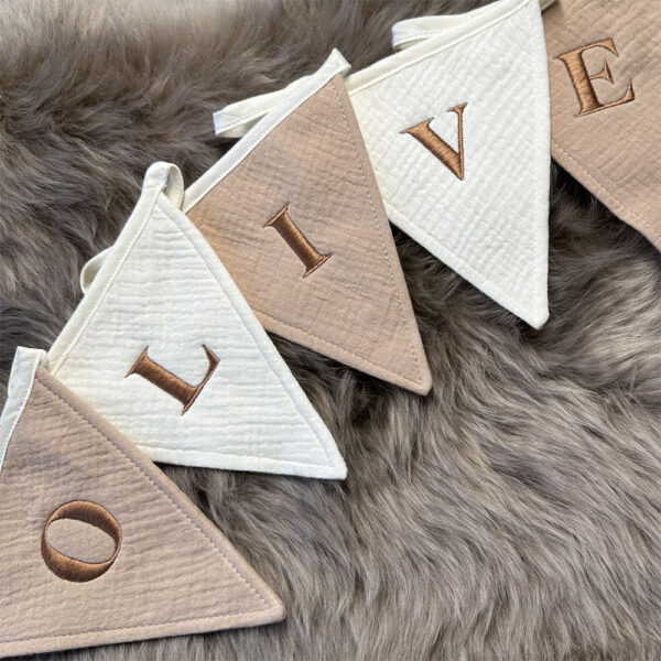 Vlaggenlijn met de naam ‘Olive’ in geborduurde koper/bruine letters, gemaakt van zacht hydrofiel katoen in beige en ivoor tinten. Slinger met naam voor verjaardagen of ter decoratie op de babykamer.